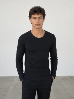 A man in a plain black long-sleeve top against a white wall, before the AI clothes changer swaps the outfit