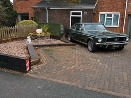The same driveway with a dark green classic fastback coupé in place of the silver car, after AI image replacement