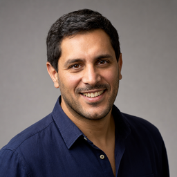 A smiling man in a navy shirt against a gray studio wall, a sample photo to whiten teeth in.