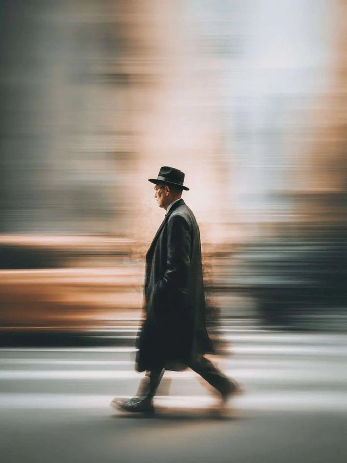 A man in a long coat crossing the street while the taxi and buildings behind him streak sideways in panning blur. A man in a long coat crossing the street while the taxi and buildings behind him streak sideways in panning blur.