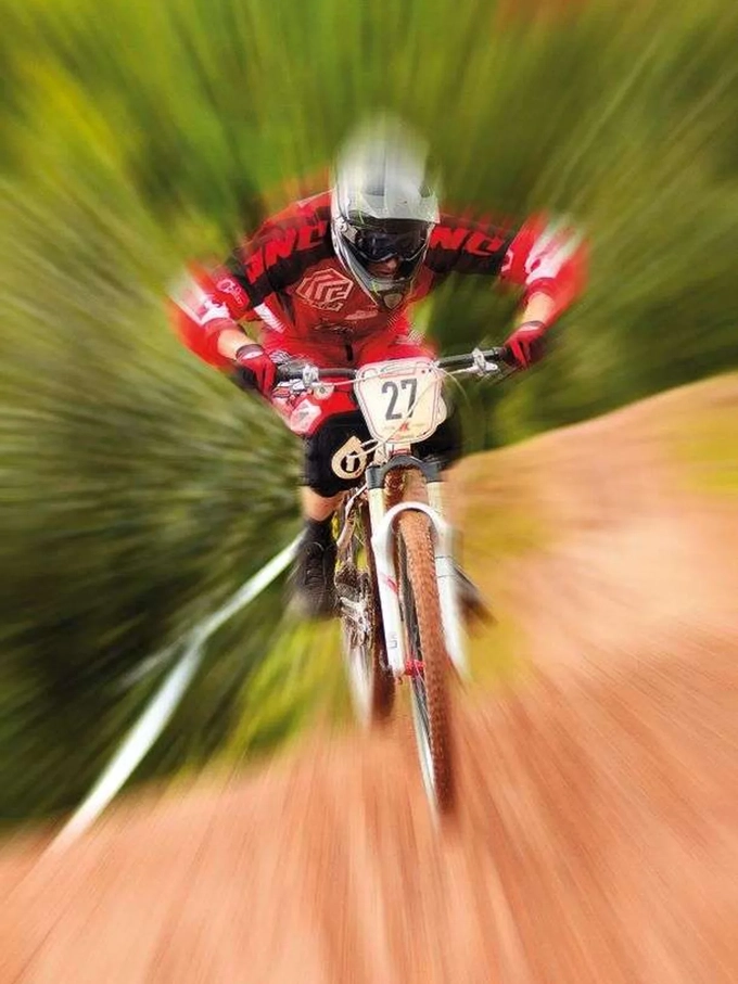 A mountain biker racing down a dirt track toward the camera, with zoom burst streaks flying out from the center. A mountain biker racing down a dirt track toward the camera, with zoom burst streaks flying out from the center.