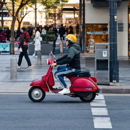 A scooter rider on a city street, side-on, a sample photo for panning motion blur.