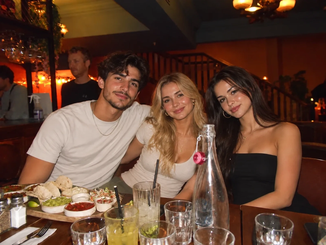 Three friends at a candle-lit bar table with a man standing behind them, before removing the person from the photo
