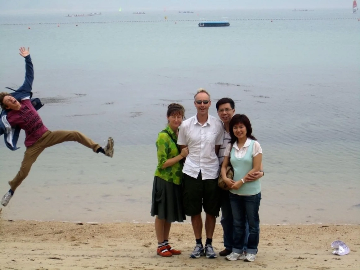 Four friends posing on a beach while a man jumps into the frame on the left, before removing the photobomber Four friends posing on a beach while a man jumps into the frame on the left, before removing the photobomber